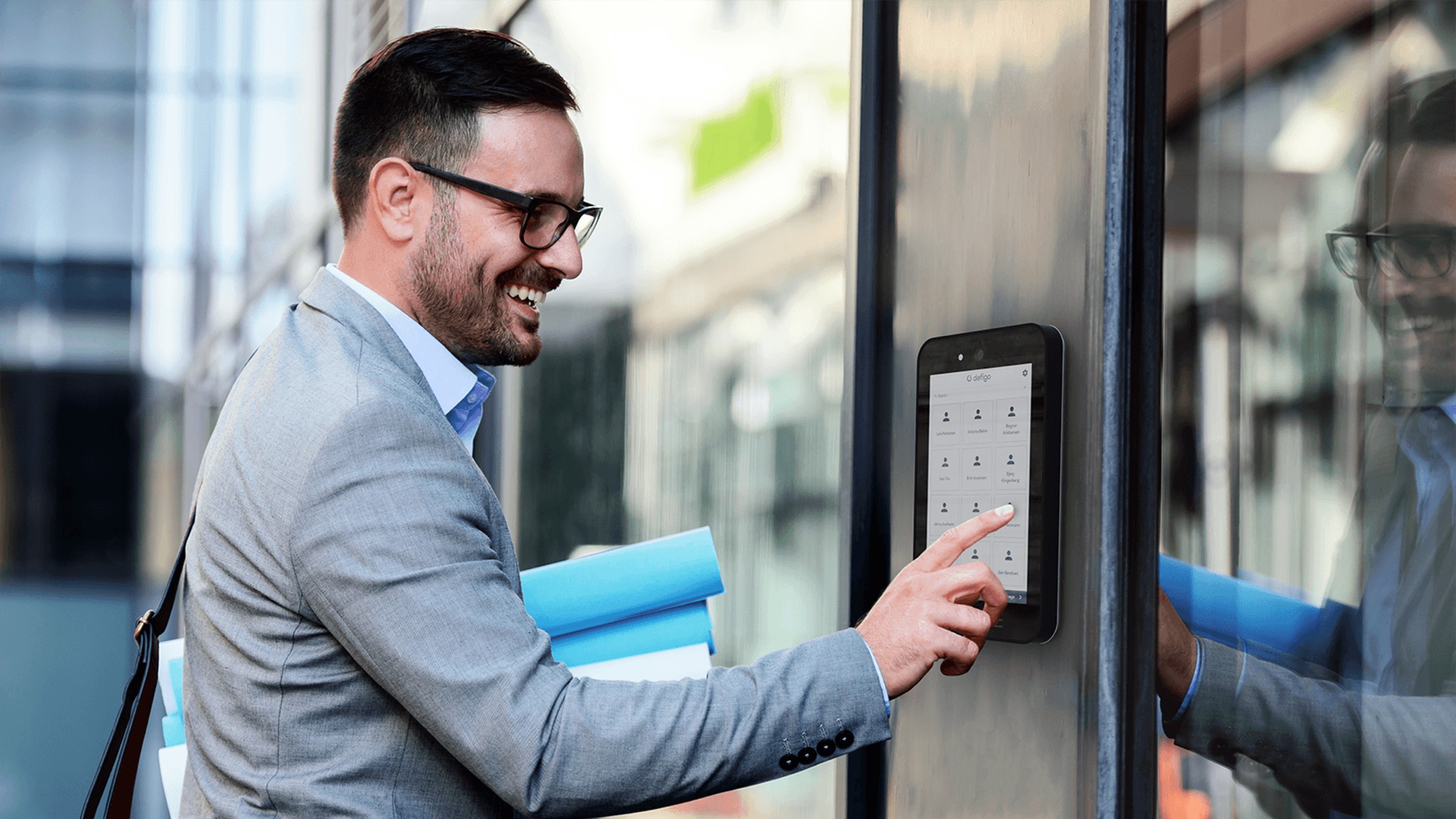 A smiling man tapping the Defigo smart intercom screen at a building entrance