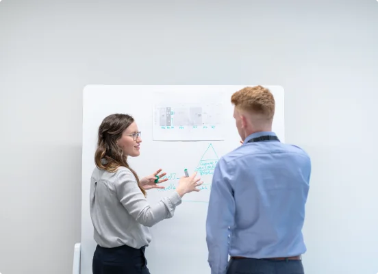 Zwei Personen diskutieren Qualitätsprüfung und Testen unter Verwendung einer Tafel in einem weißen Raum