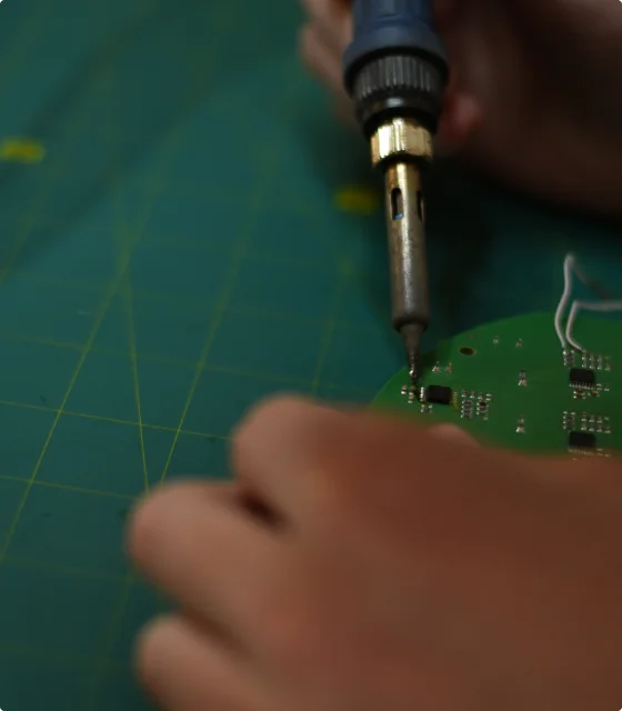 a hand holding a soldering Iron working on a green hardware on a flat surface