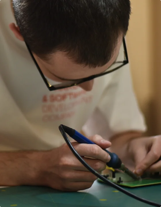 En mann med briller jobber manuelt med maskinvare ved hjelp av verktøy som loddejern